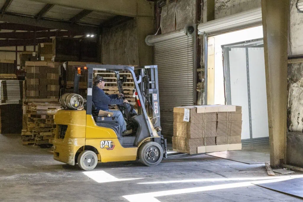 man driving forklift carrying cardboard bulk stacks of cardboard boxes