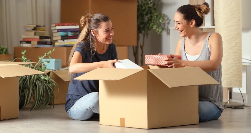 two women sitting unpacking a cardboard box