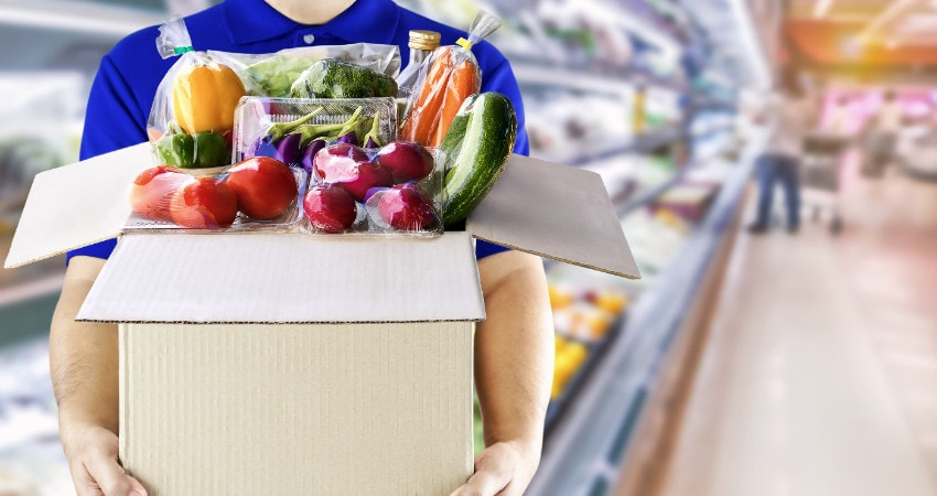 man holding cardboard box full of vegetables grocery store