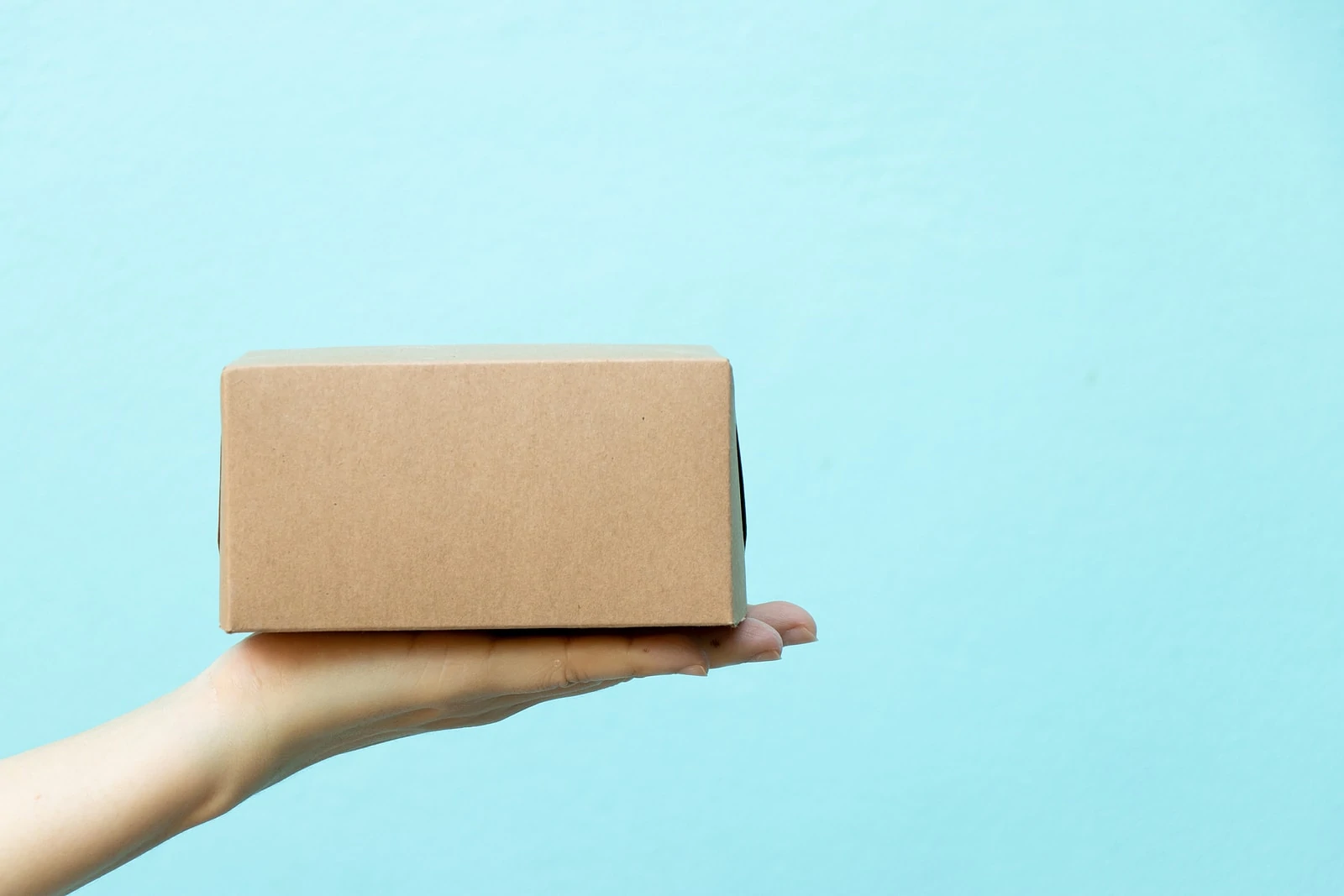 Woman hand hold the brown corrugated box on blue wall background with copy space