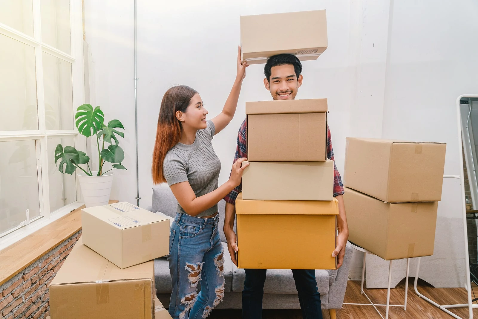 happy young couple carrying big cardboard box for moving in new house