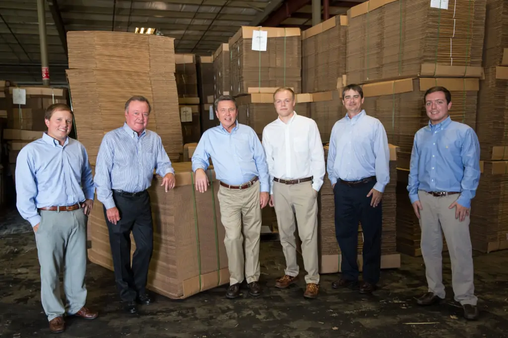 Group picture of staff in front of stacks of corrugated cardboard